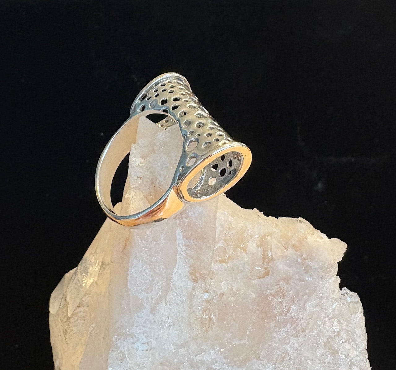 Silver ring with textured design on a crystal base against a black background
