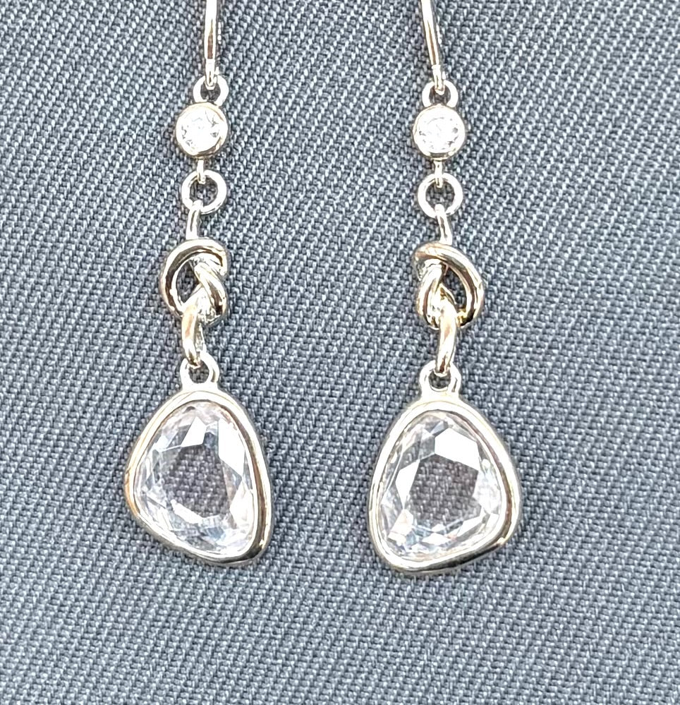 Silver earrings with teardrop-shaped clear gemstones on a gray textured background