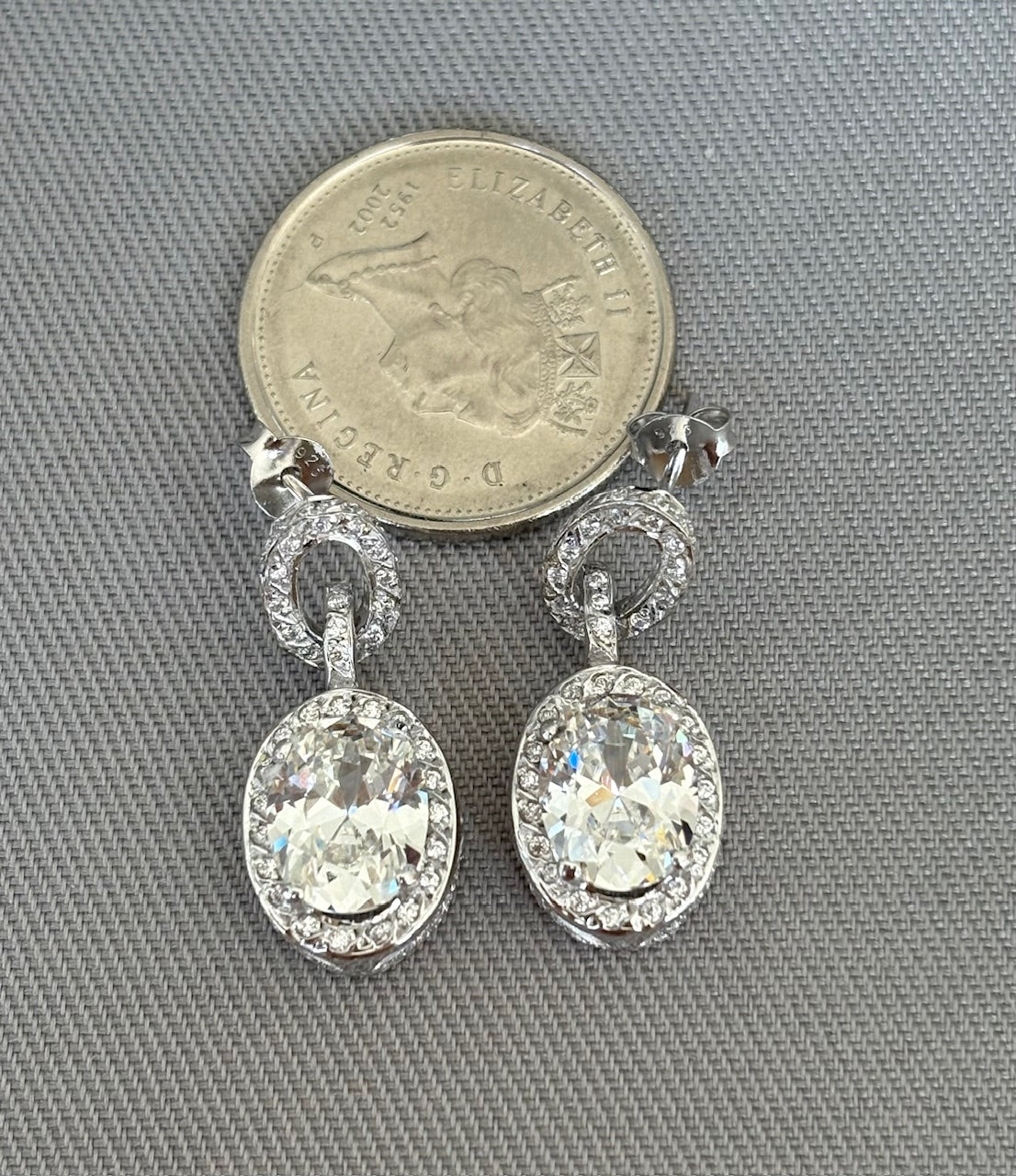 Pair of silver earrings with large central stones, shown next to a coin for scale on a gray background.