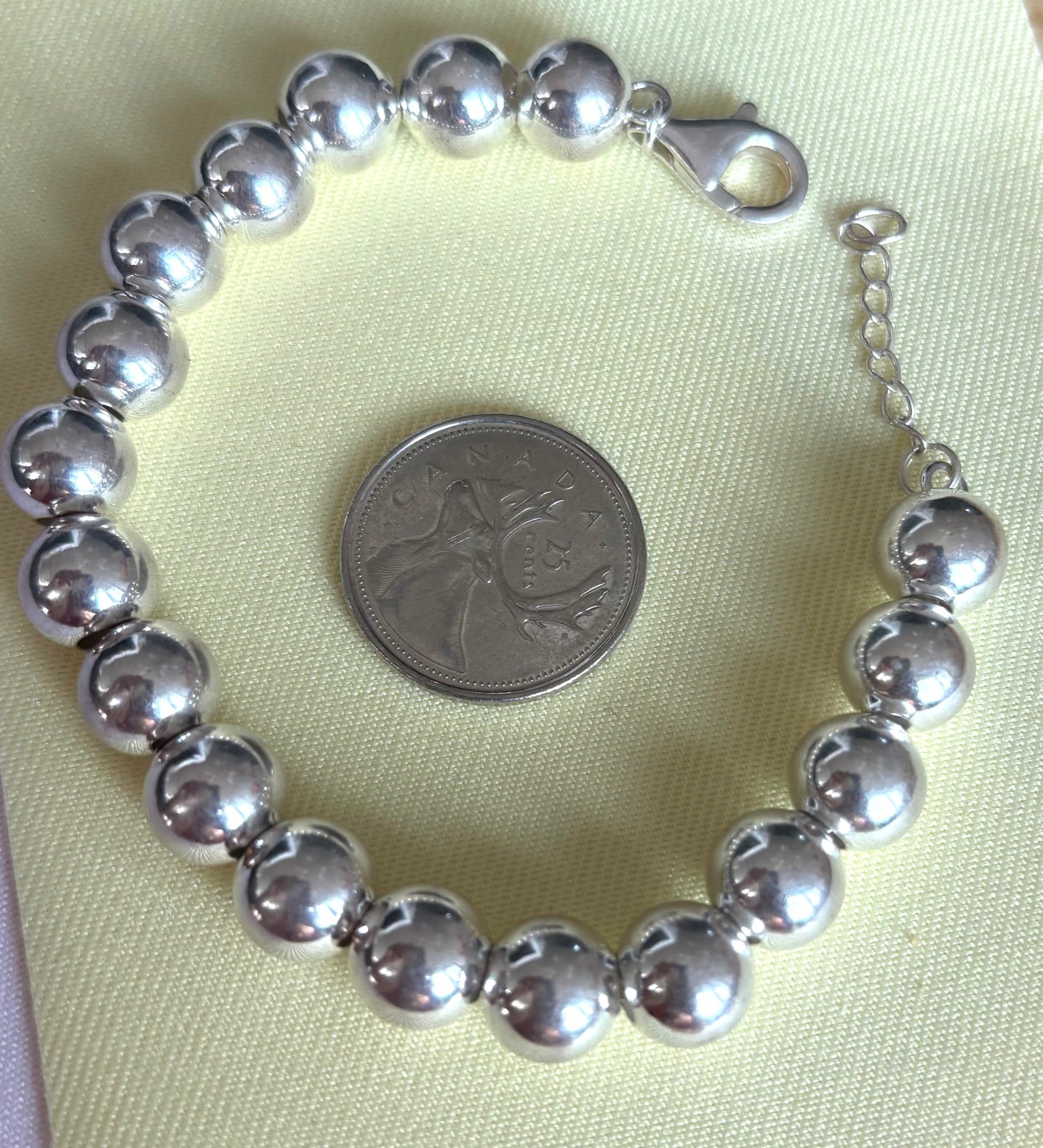 Silver beaded ball bracelet on a light green fabric background with a coin for scale.