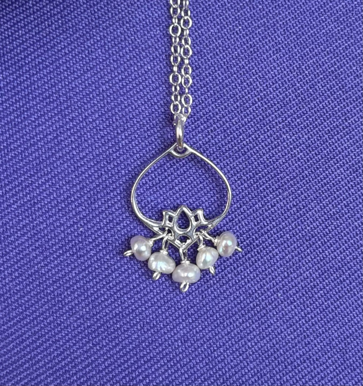 Silver necklace with a pendant featuring five pearls on a blue textured background