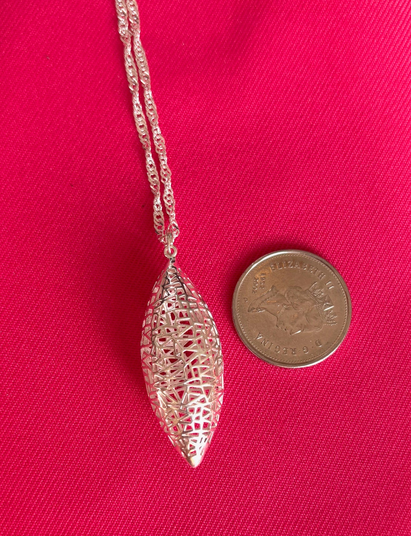 Silver pod-shaped pendant necklace on a pink background with a coin for scale.