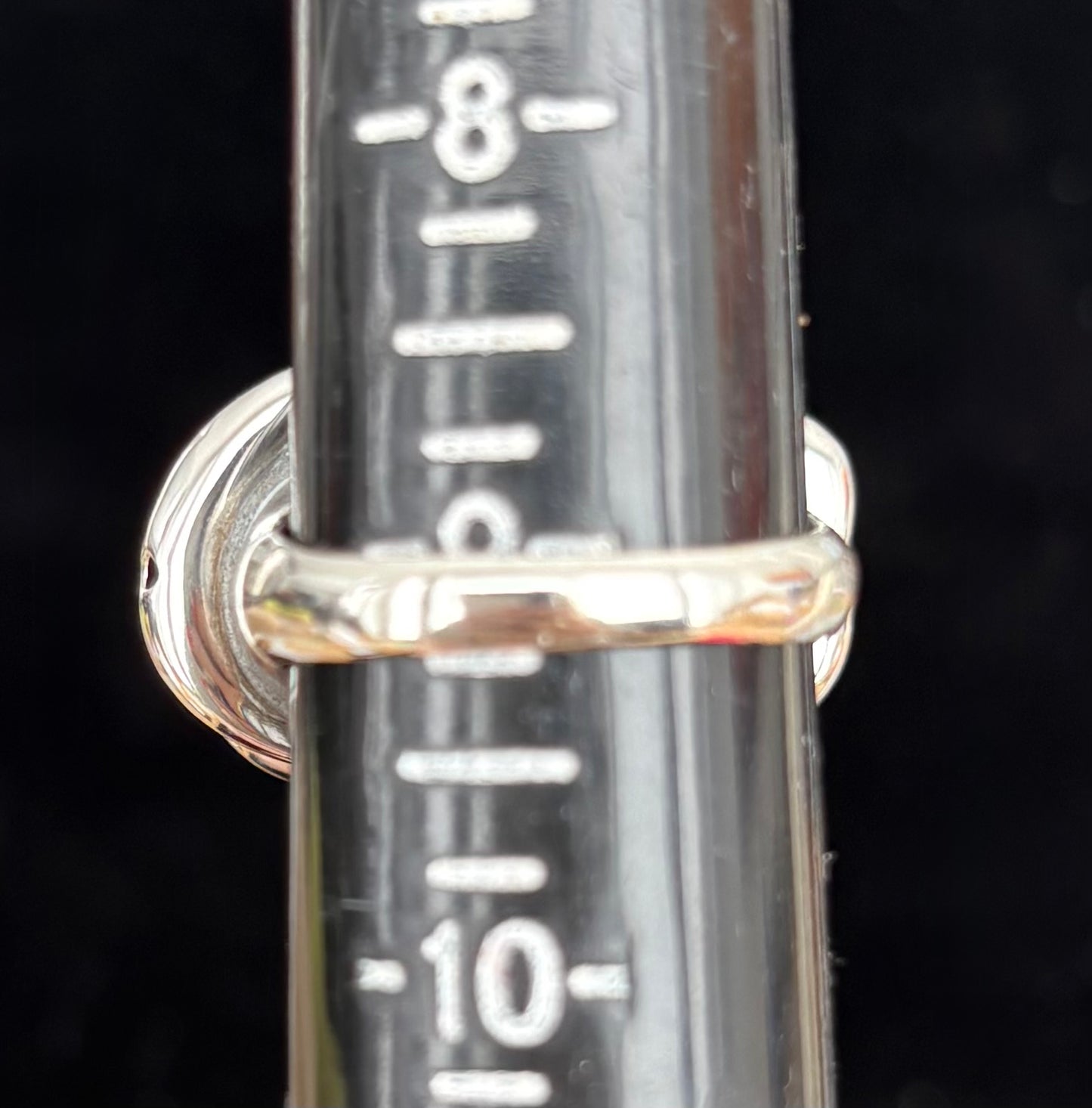 Silver ring with a cylindrical metal component featuring measurement markings on a black background