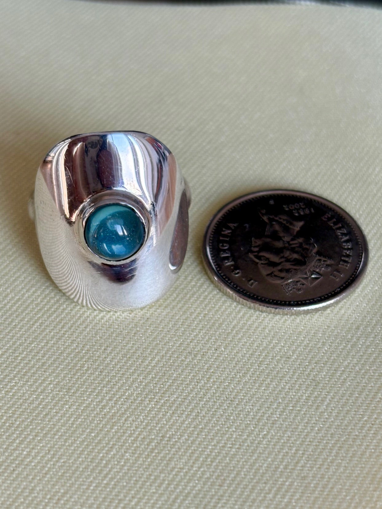 Silver ring with a blue topaz gemstone next to a U.S. quarter on a beige fabric background