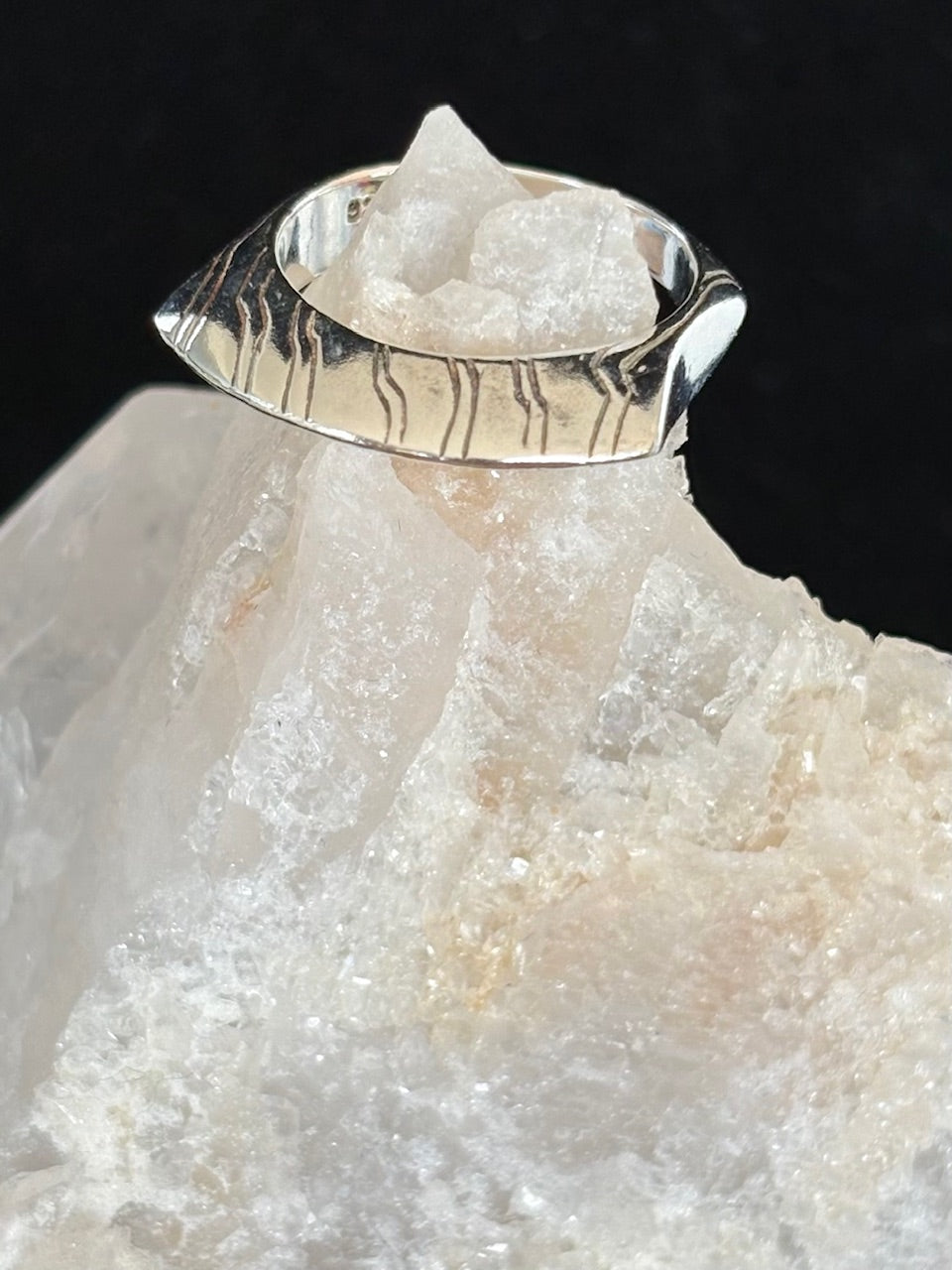 Silver ring on a crystal rock with a black background