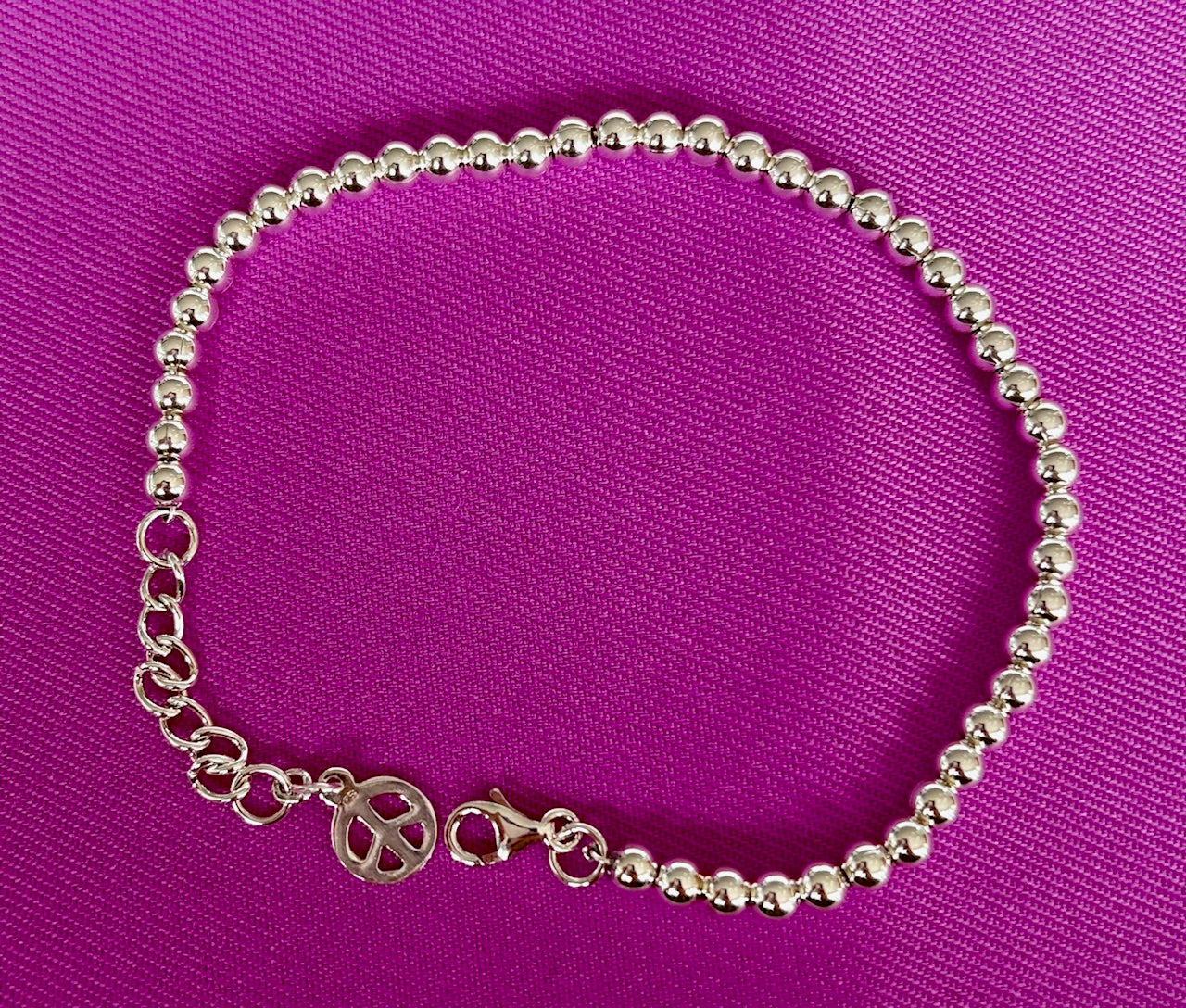 Jolie Esprit Sterling Silver beaded ball bracelet with a peace sign charm on a purple background