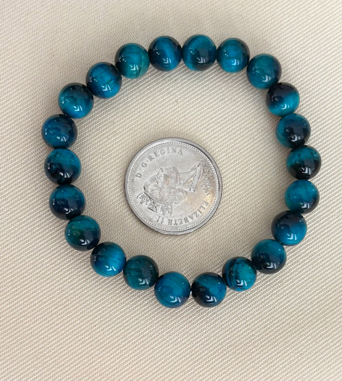 Blue gemstone bracelet next to a silver coin on a beige background