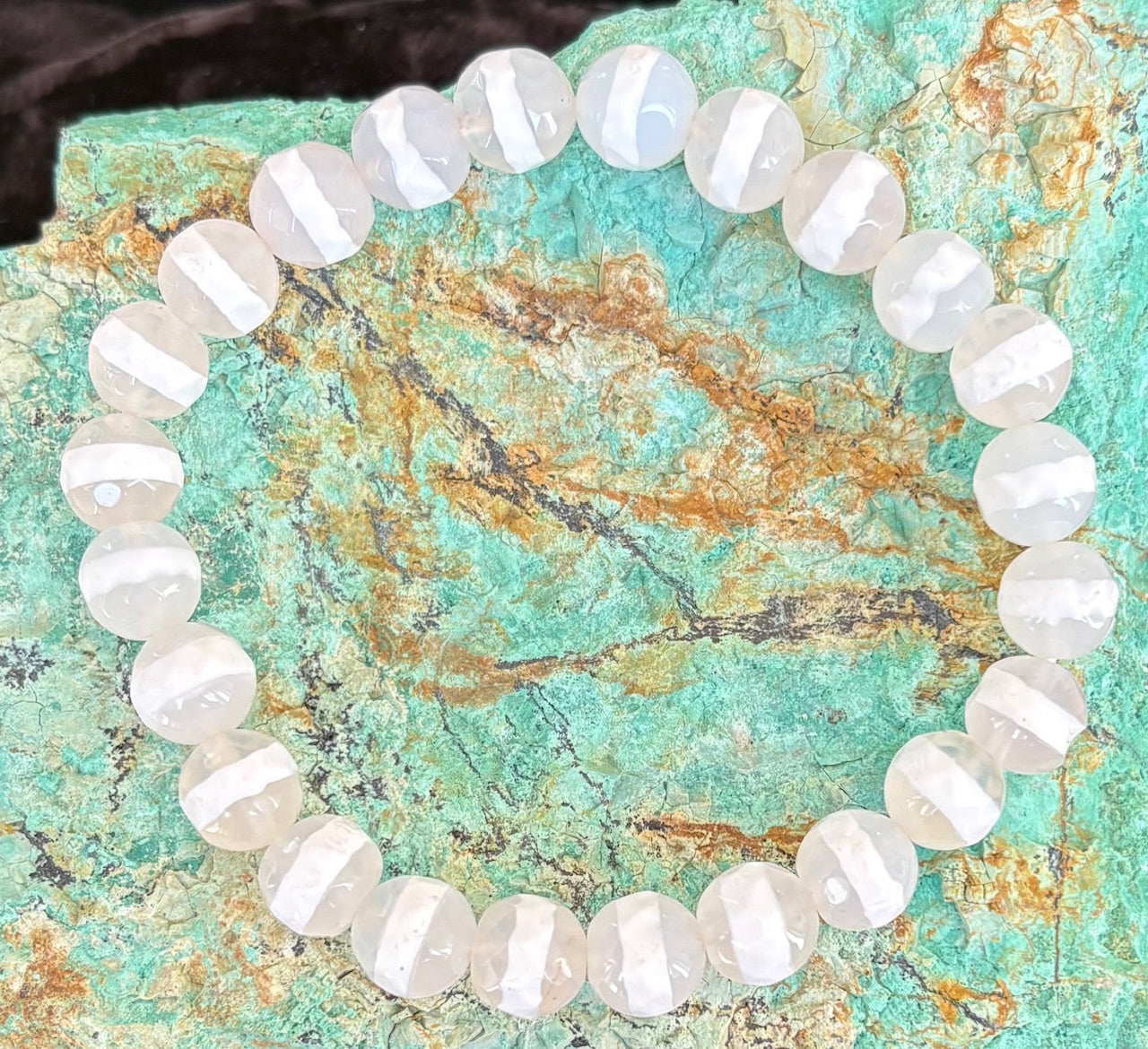 White gemstone beaded bracelet on a textured green stone surface