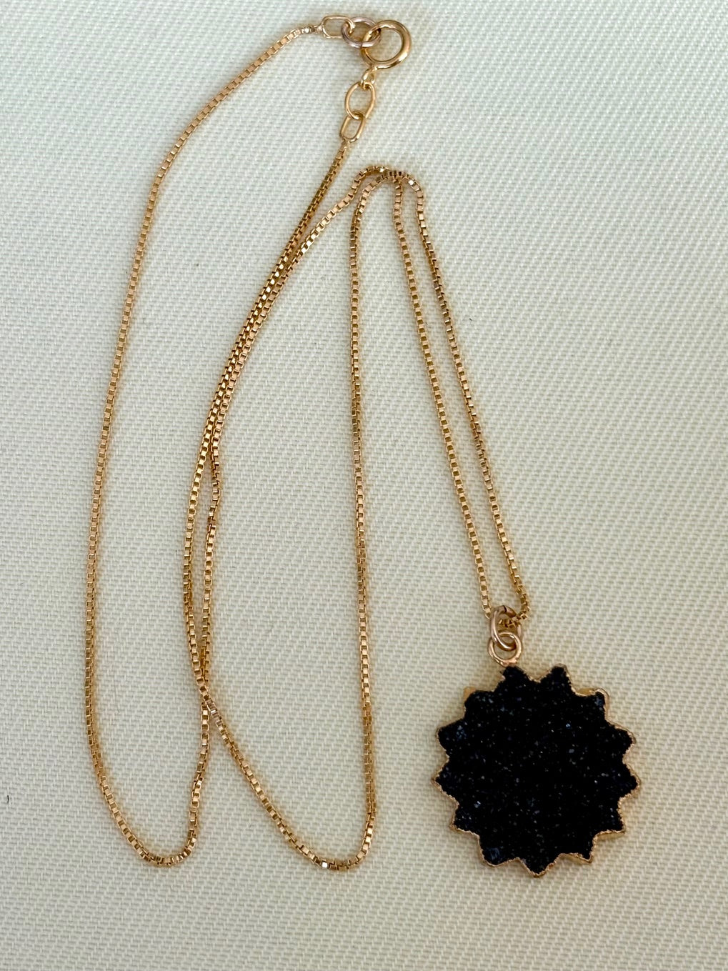 Gold necklace with a black pendant on a light beige background