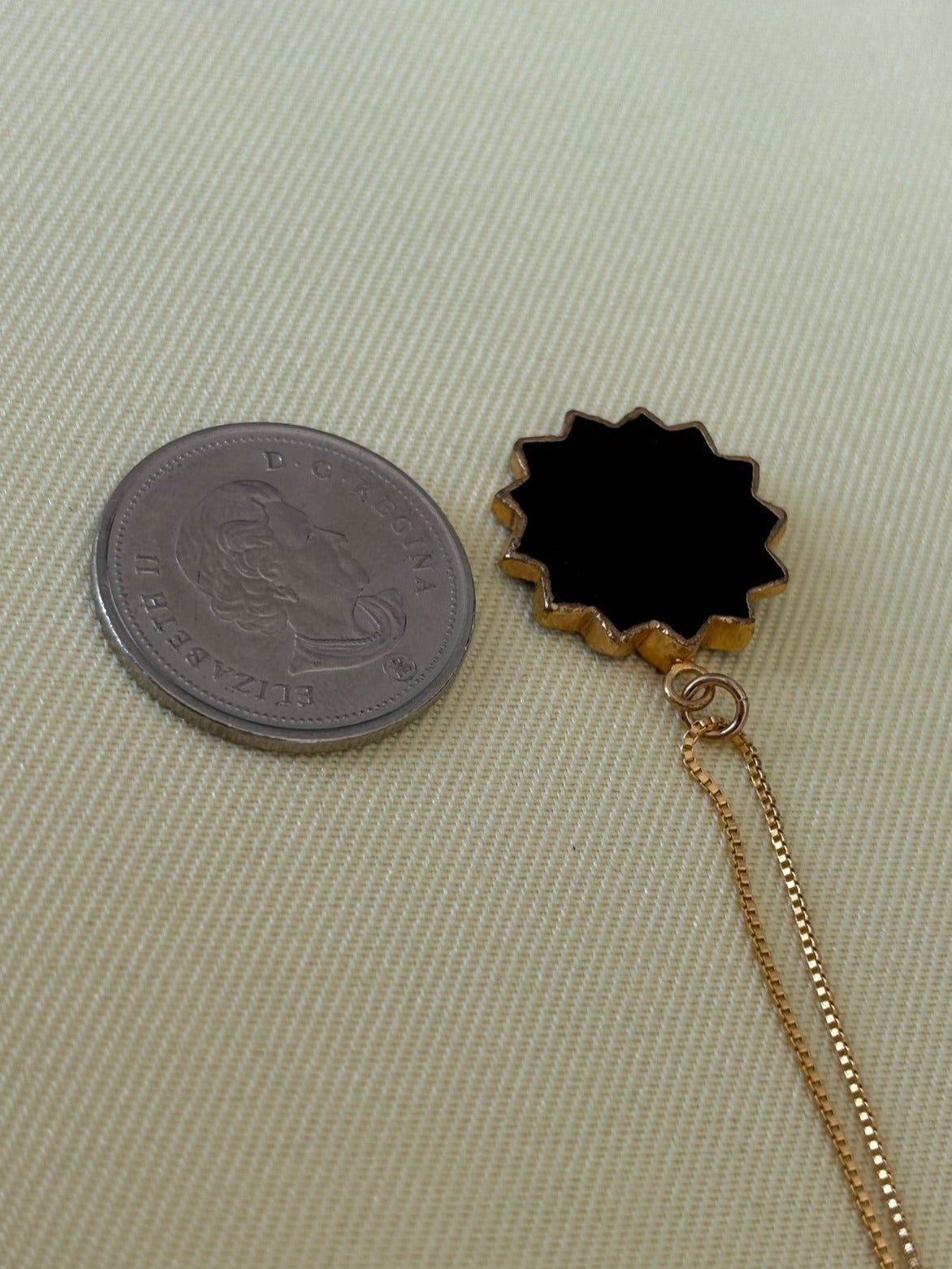 14Kt Gold Fill necklace with a black druzy sunburst pendant on a light green fabric surface
