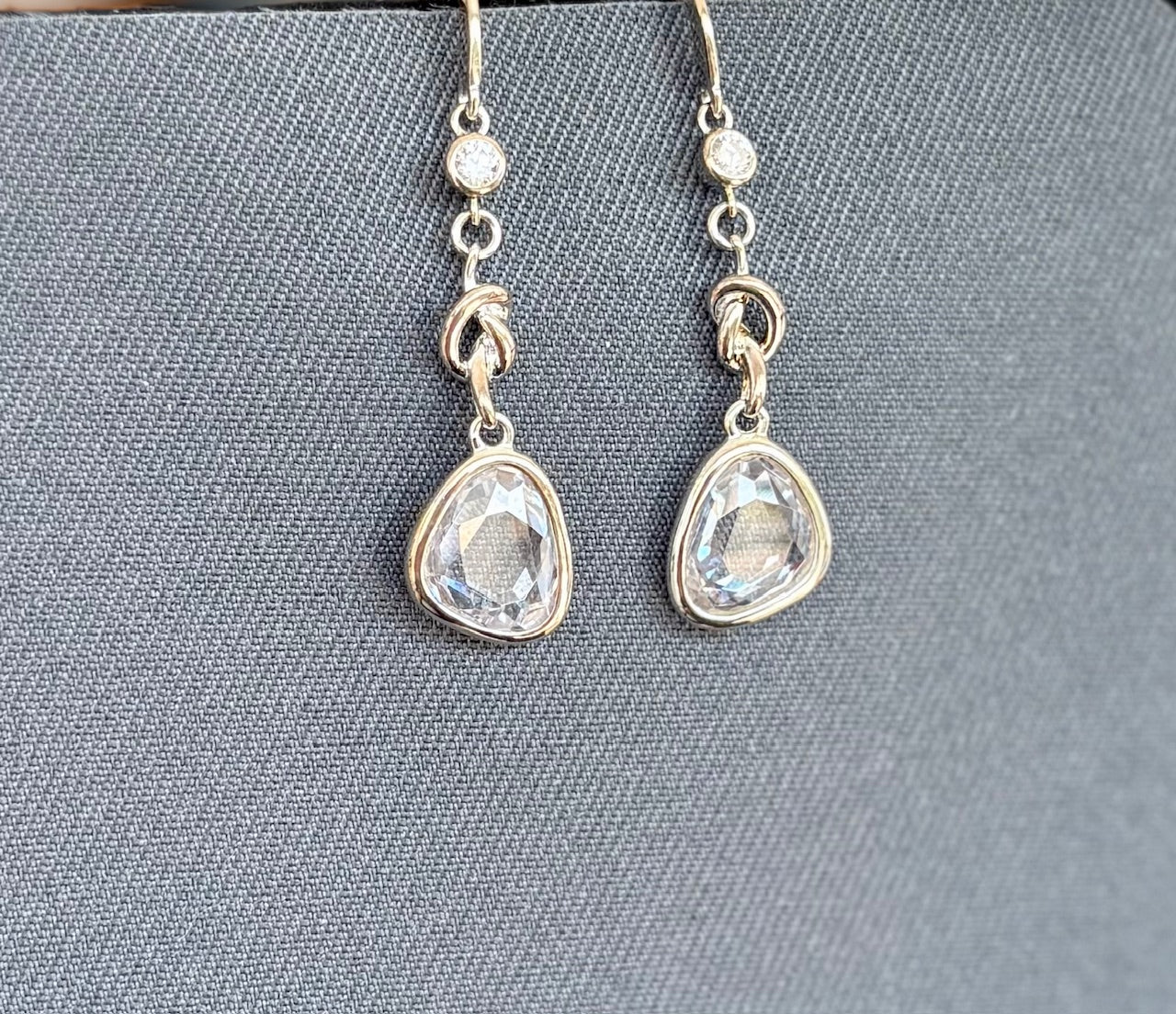 Silver teardrop earrings with clear gemstones on a gray fabric background