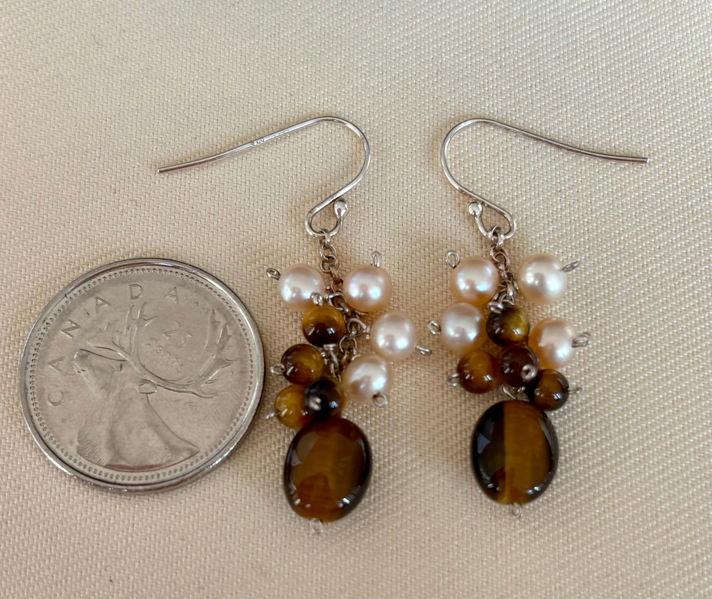 Pair of earrings with Tigers eye and pearl beads next to a Canadian quarter on a beige background
