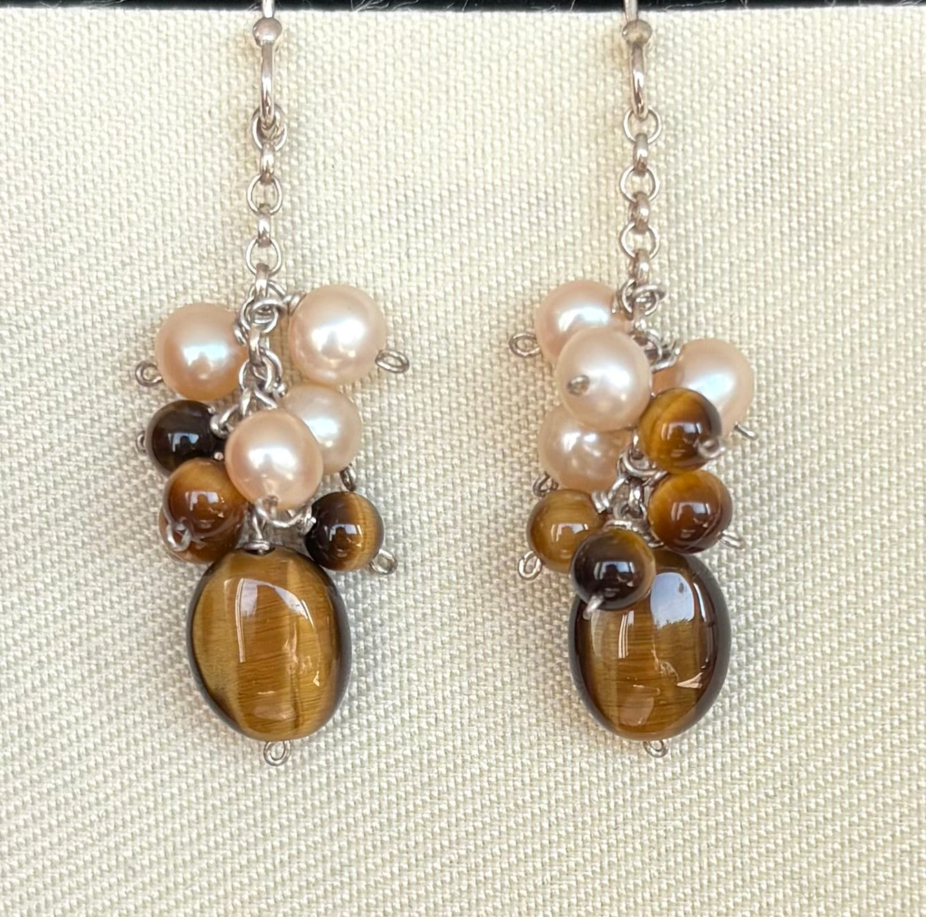 Pair of earrings with pearls and tiger's eye stones on a beige background