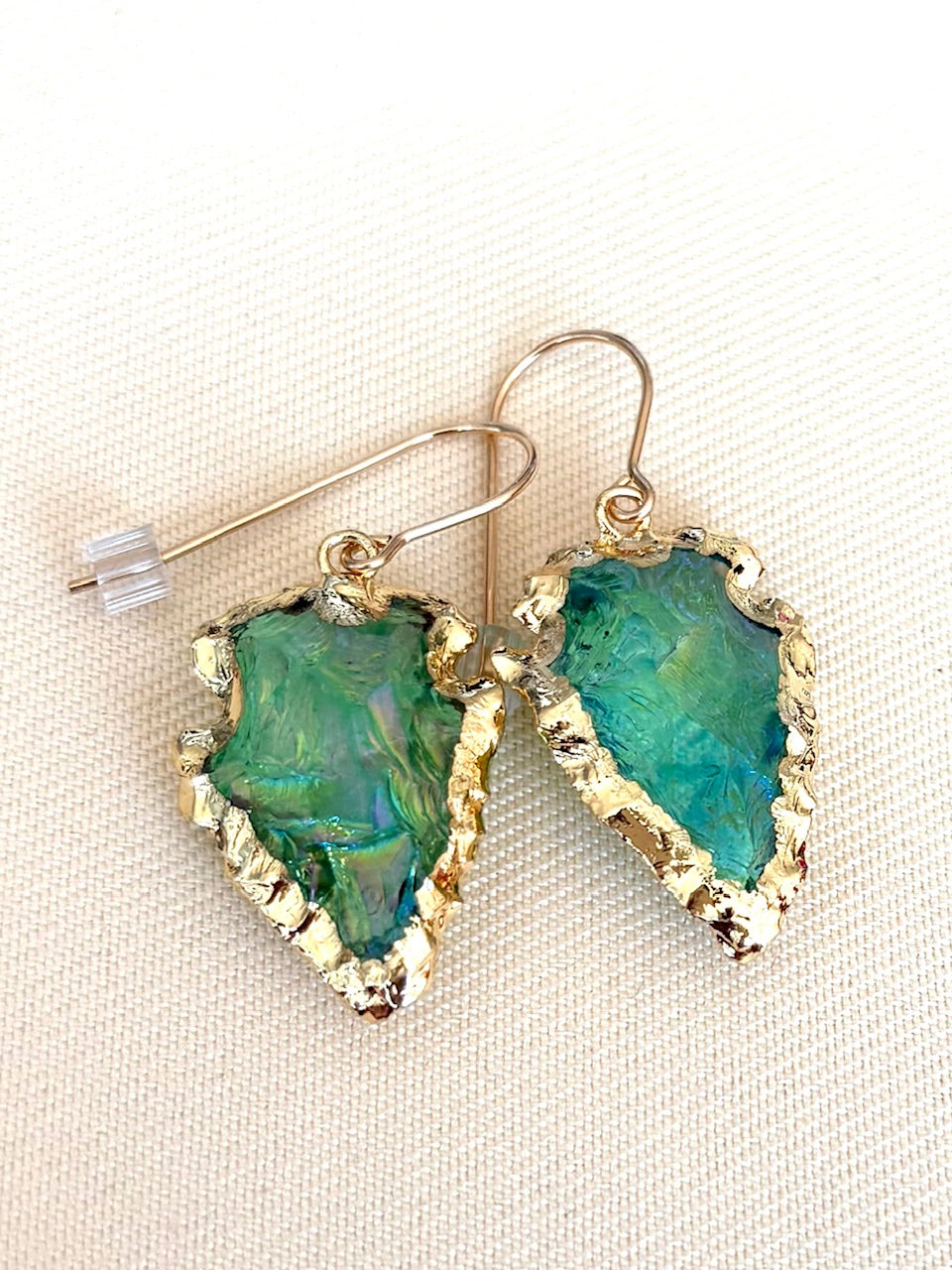 Jolie Esprit green gemstone earrings with gold accents on a beige fabric background