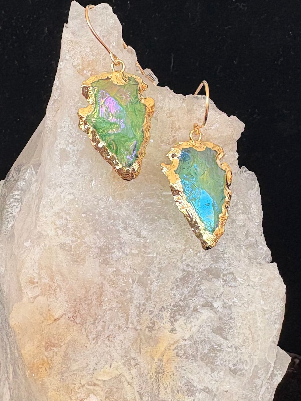 Jolie Esprit Titanium coated green quartz earrings with gold frames on a rock background