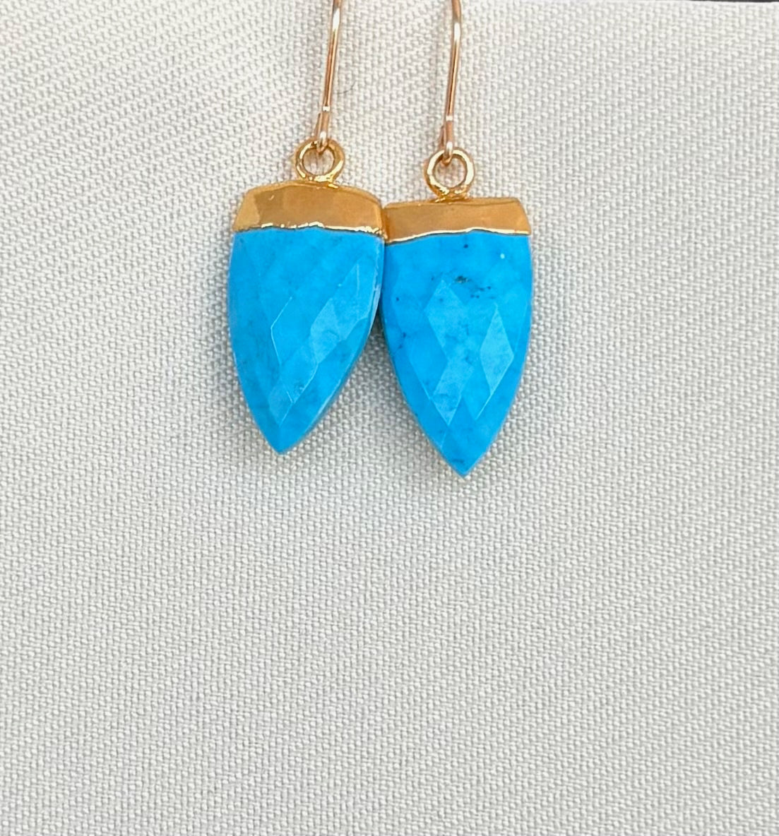 Blue earrings with gold tops on a light gray background