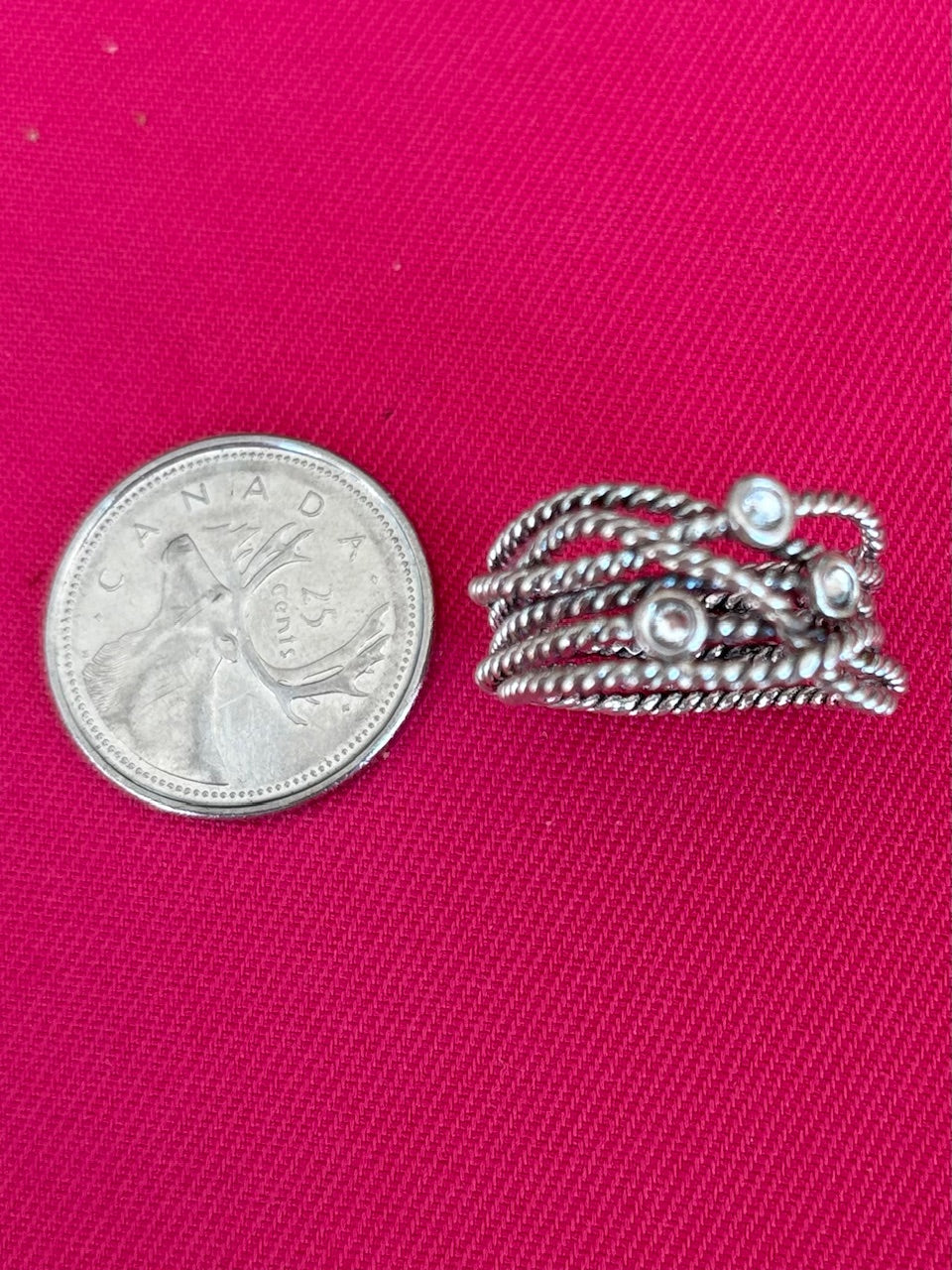 Silver ring with crystals next to a quarter on a pink background