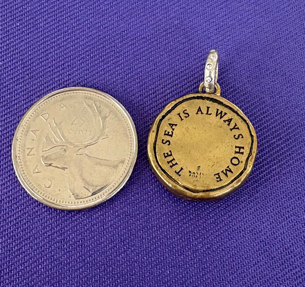 Sterling and brass pendant with 'The Sea is Always Home' inscription next to a Canadian coin on a blue background