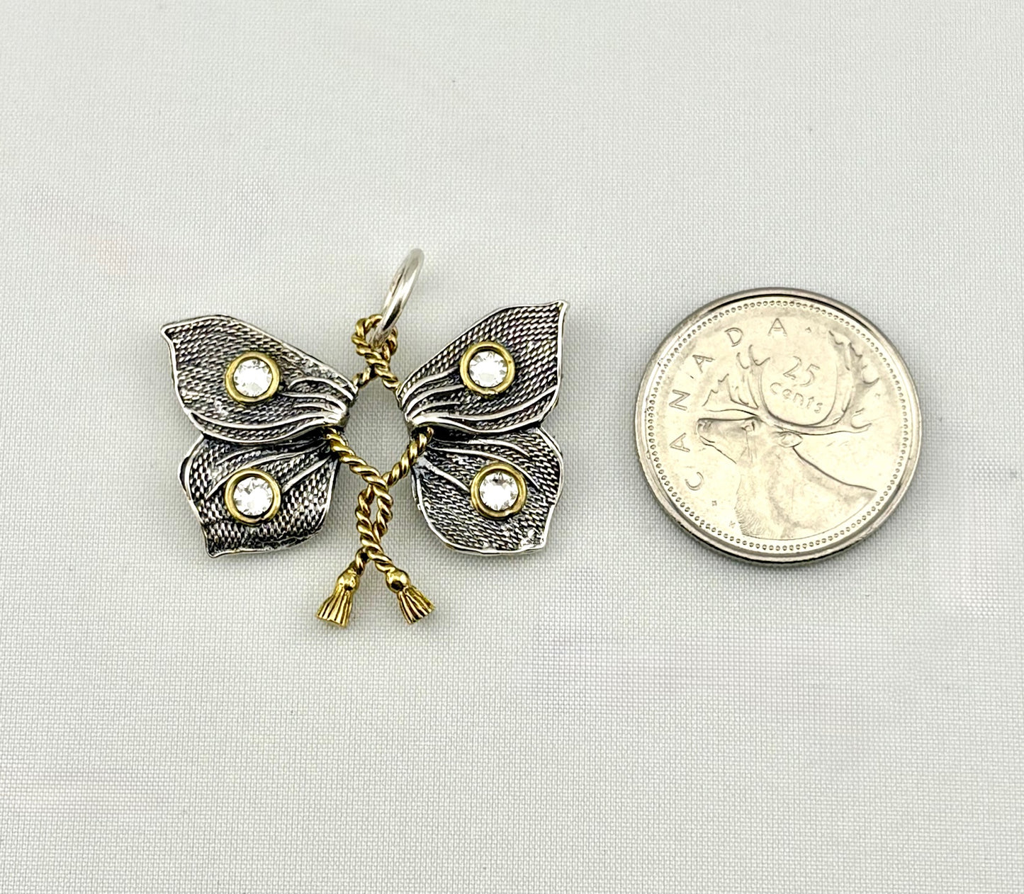 Butterfly-shaped pendant with gemstones next to a Canadian quarter coin on a light gray background