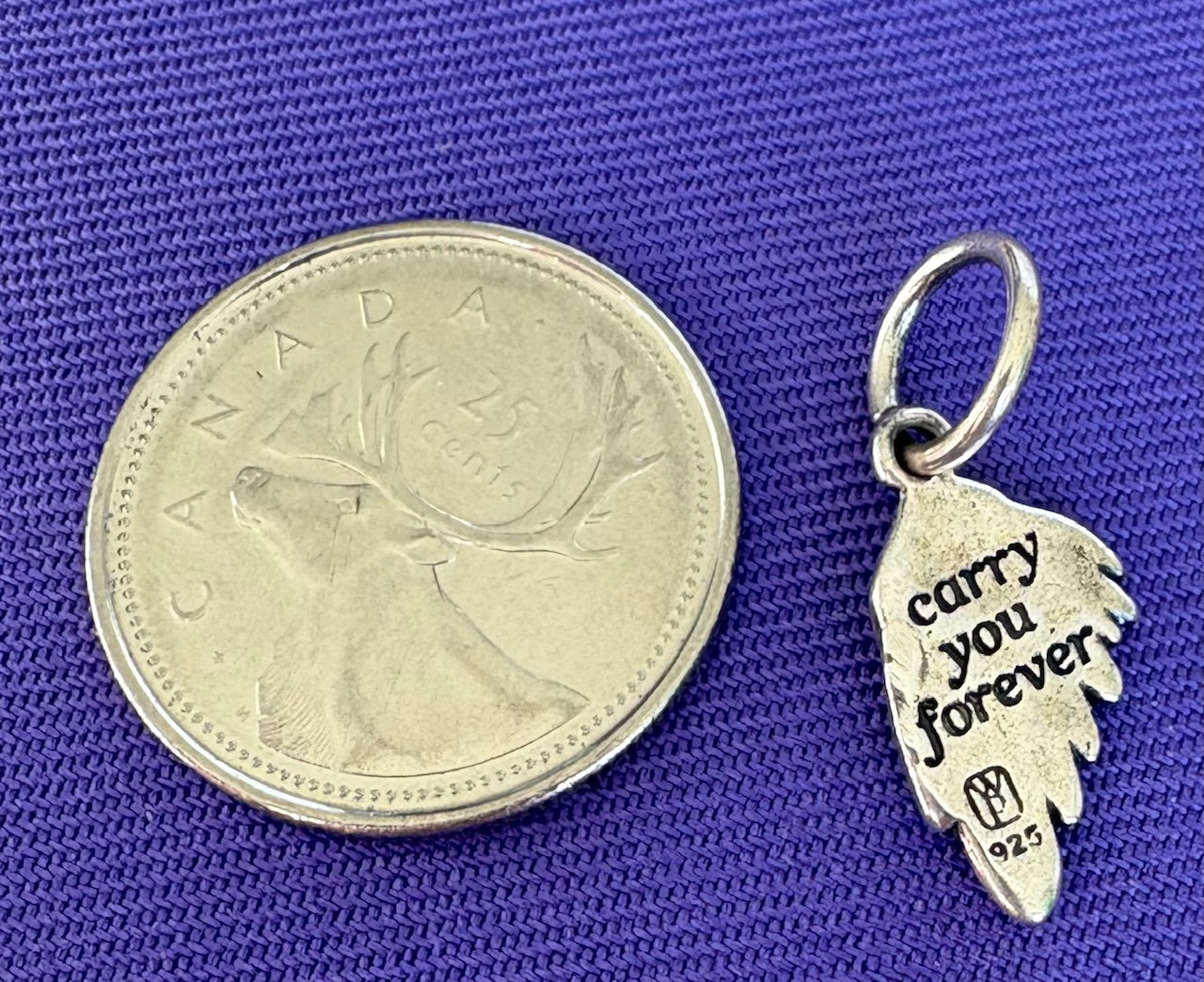 Silver 'carry you forever' pendant next to a Canadian quarter on a blue background