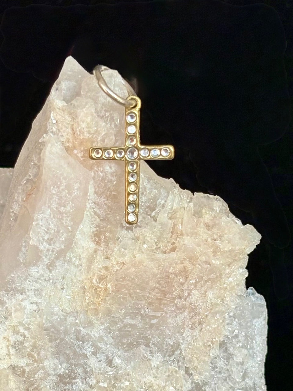 Gold cross pendant with clear stones on a crystal background