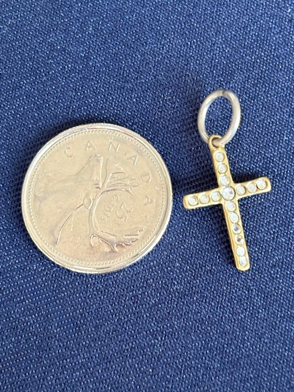 Gold cross pendant next to a Canadian coin on a blue background