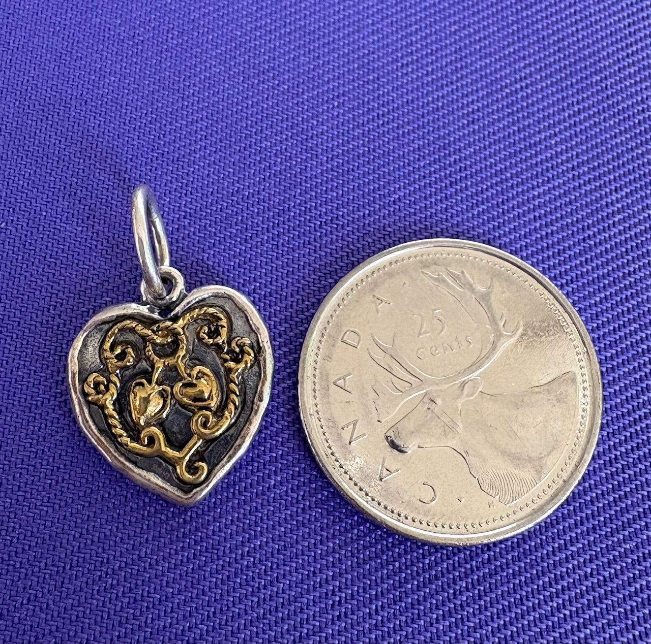 Sterling silver heart-shaped pendant with intricate design next to a Canadian coin on a blue background. Made by Waxing Poetic.