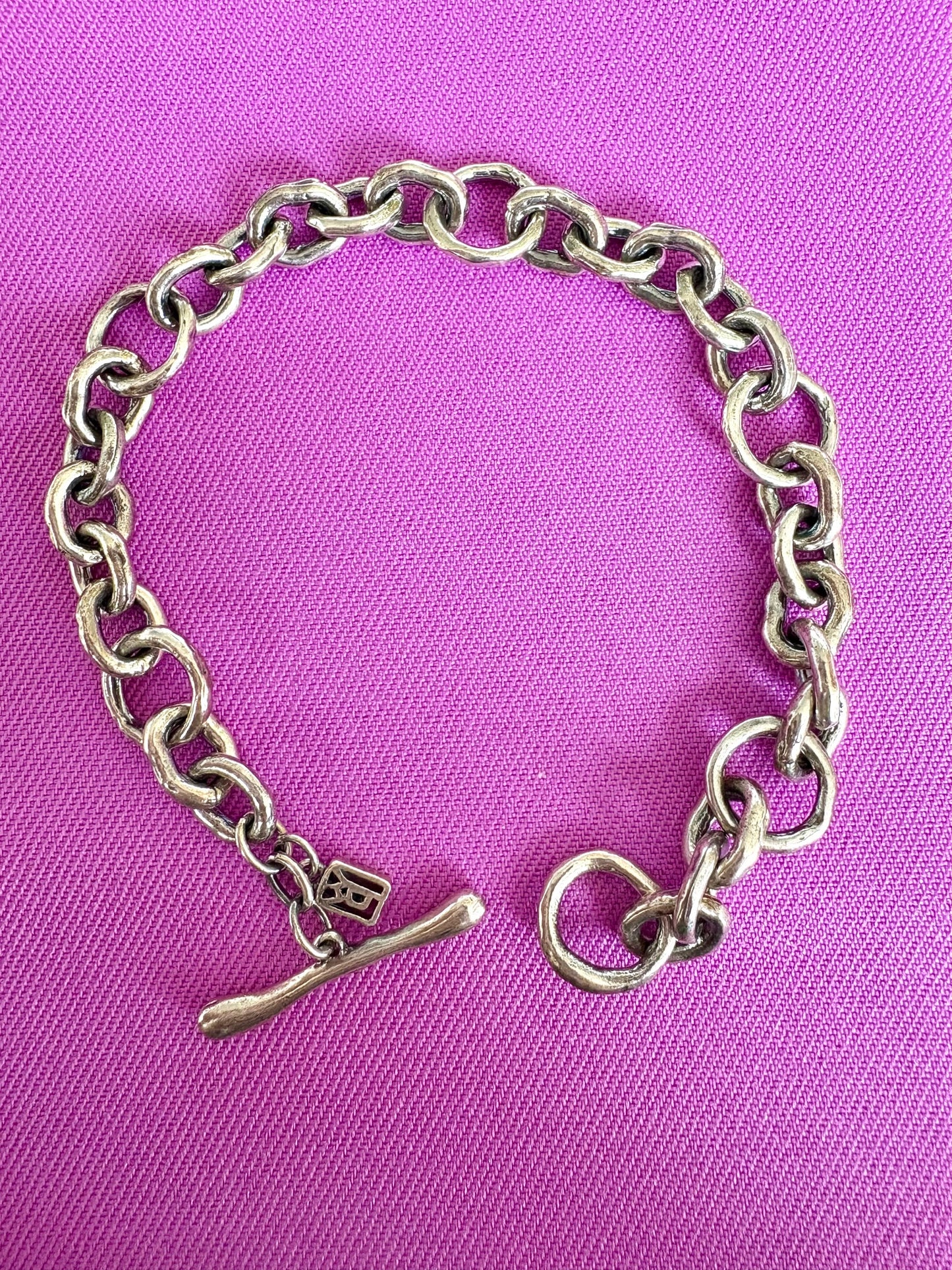 Sterling silver chain bracelet with a small charm on a purple background