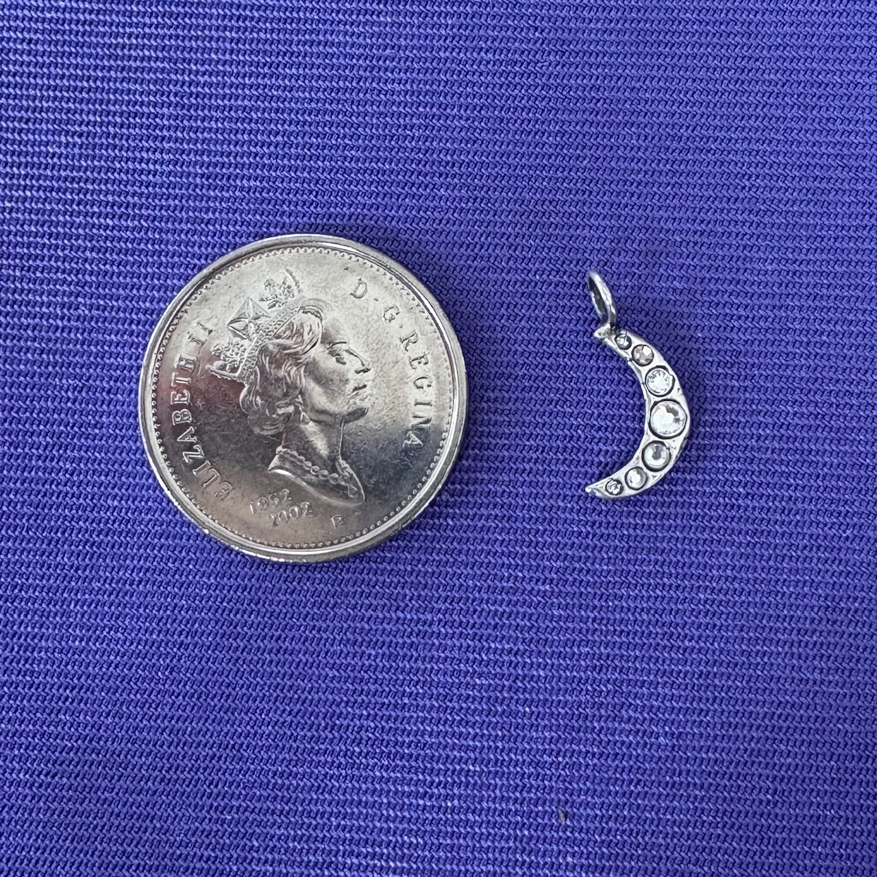 Silver crescent moon charm next to a coin on a blue background