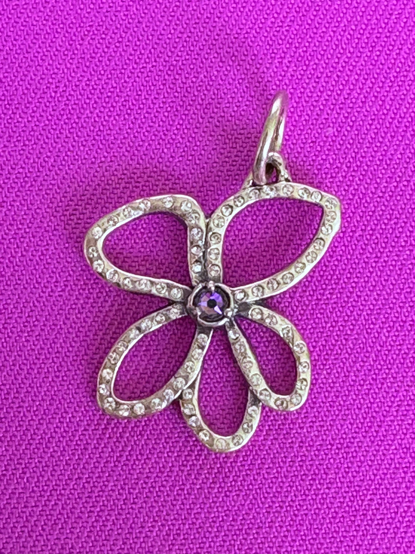 Flower-shaped pendant with a purple gemstone on a pink fabric background. Waxing Poetic