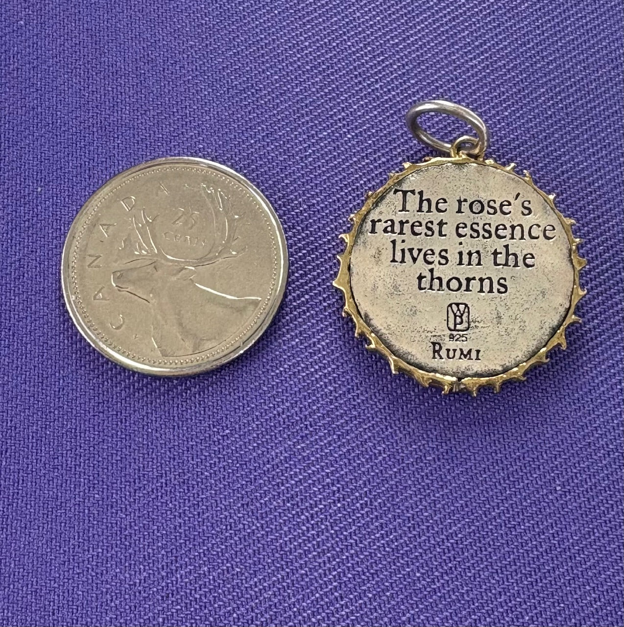 Sterling silver pendant with Rumi quote next to a coin on a purple fabric background