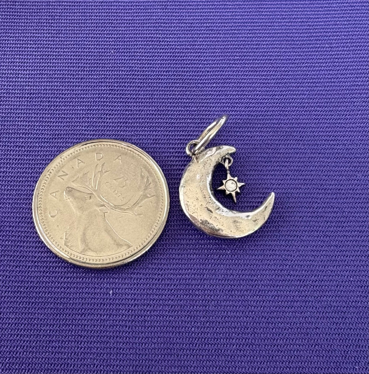 Sterling Silver moon and star charm pendant next to a coin on a blue background