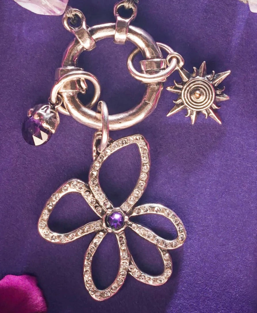 Silver necklace with a flower pendant and sun charm on a purple background