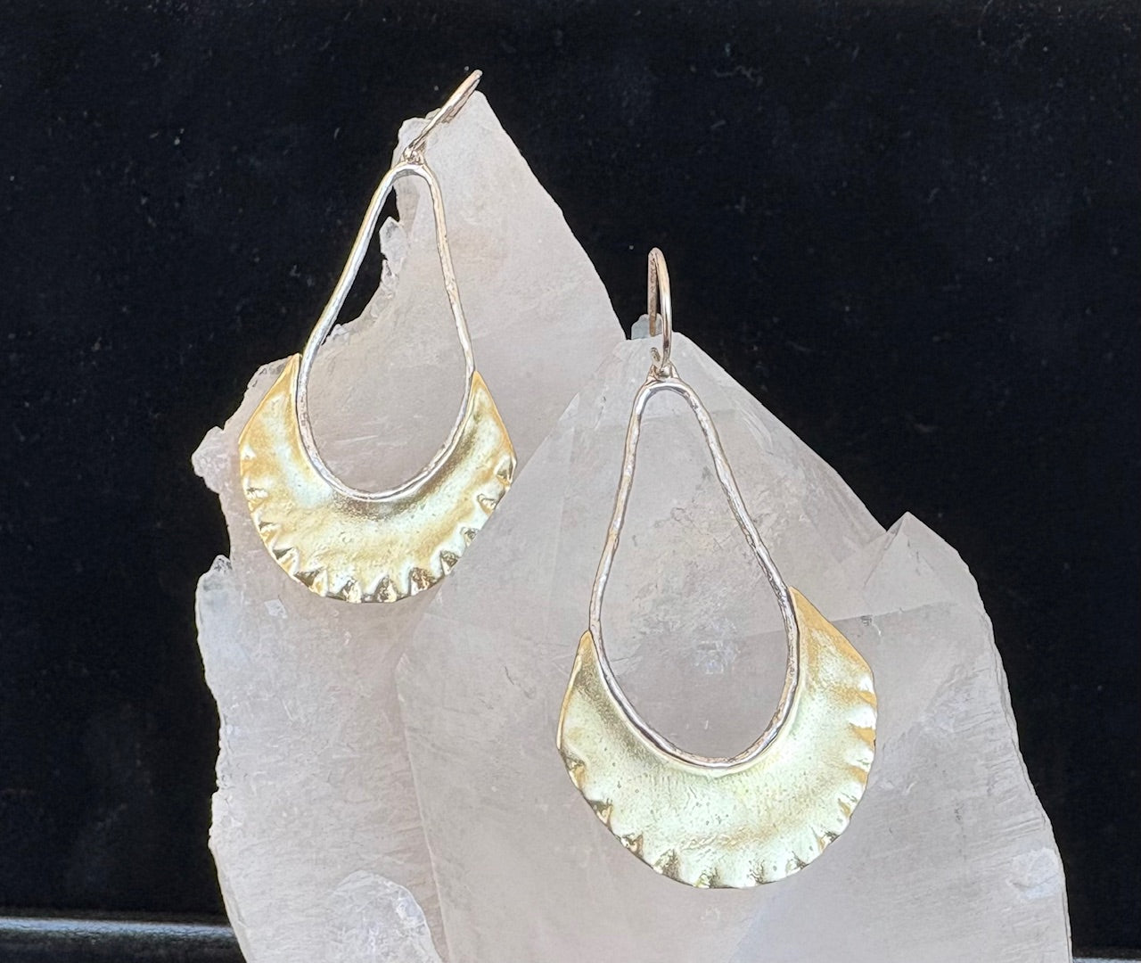Sterling and brass earrings on a clear crystal with a black background