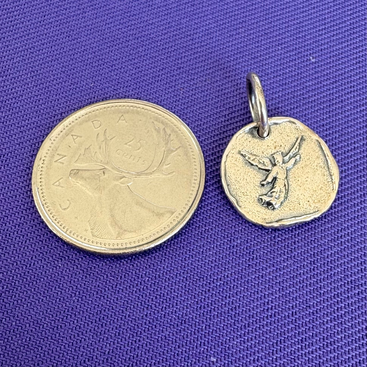 Sterling silver charm with an angel next to a Canadian quarter on a blue background