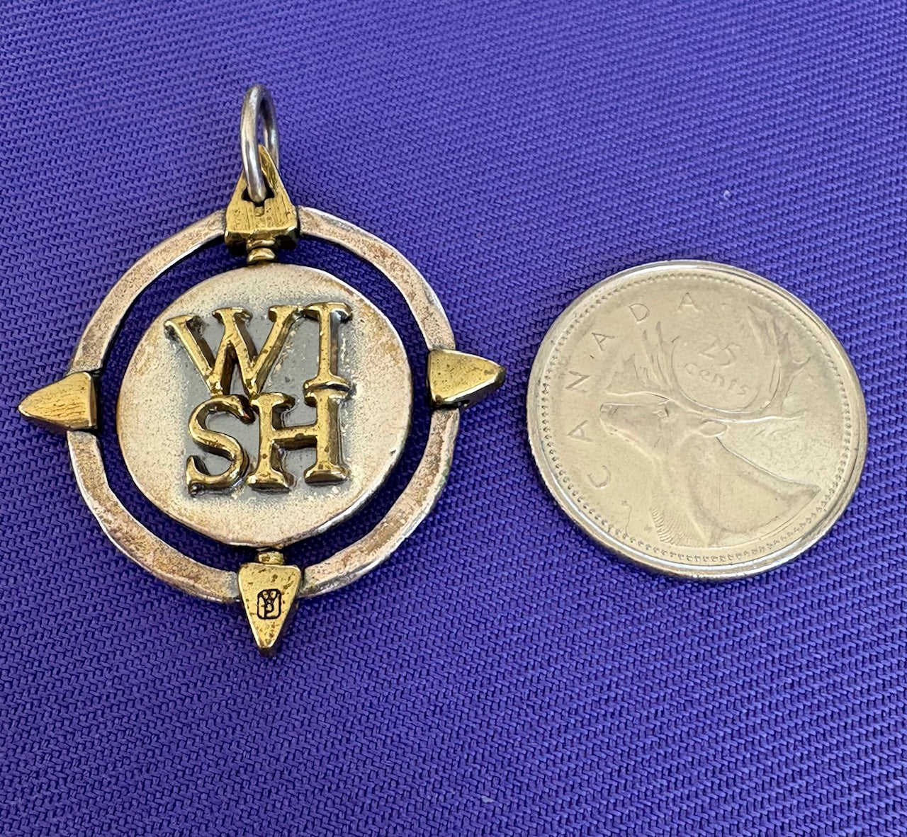 Sterling Silver pendant with 'WISH' engraving next to a coin on a blue background
