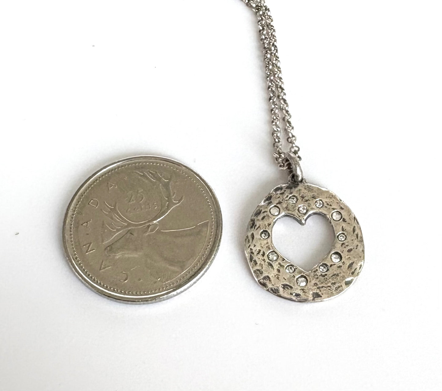 Silver necklace with a heart-shaped pendant next to a coin on a white background. Waxing Poetic
