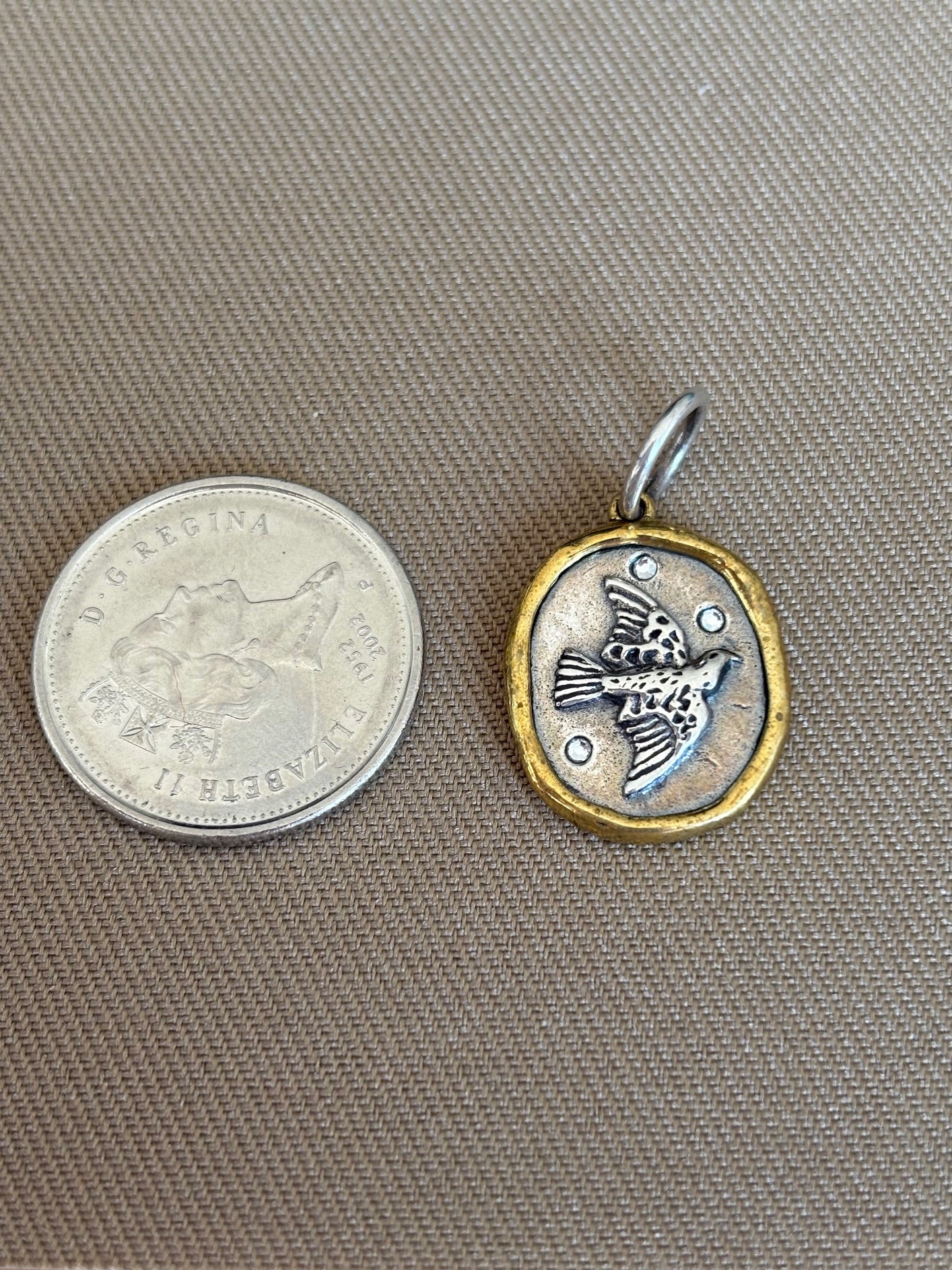 Waxing Poetic pendant with bird design next to a Canadian quarter on a gray background