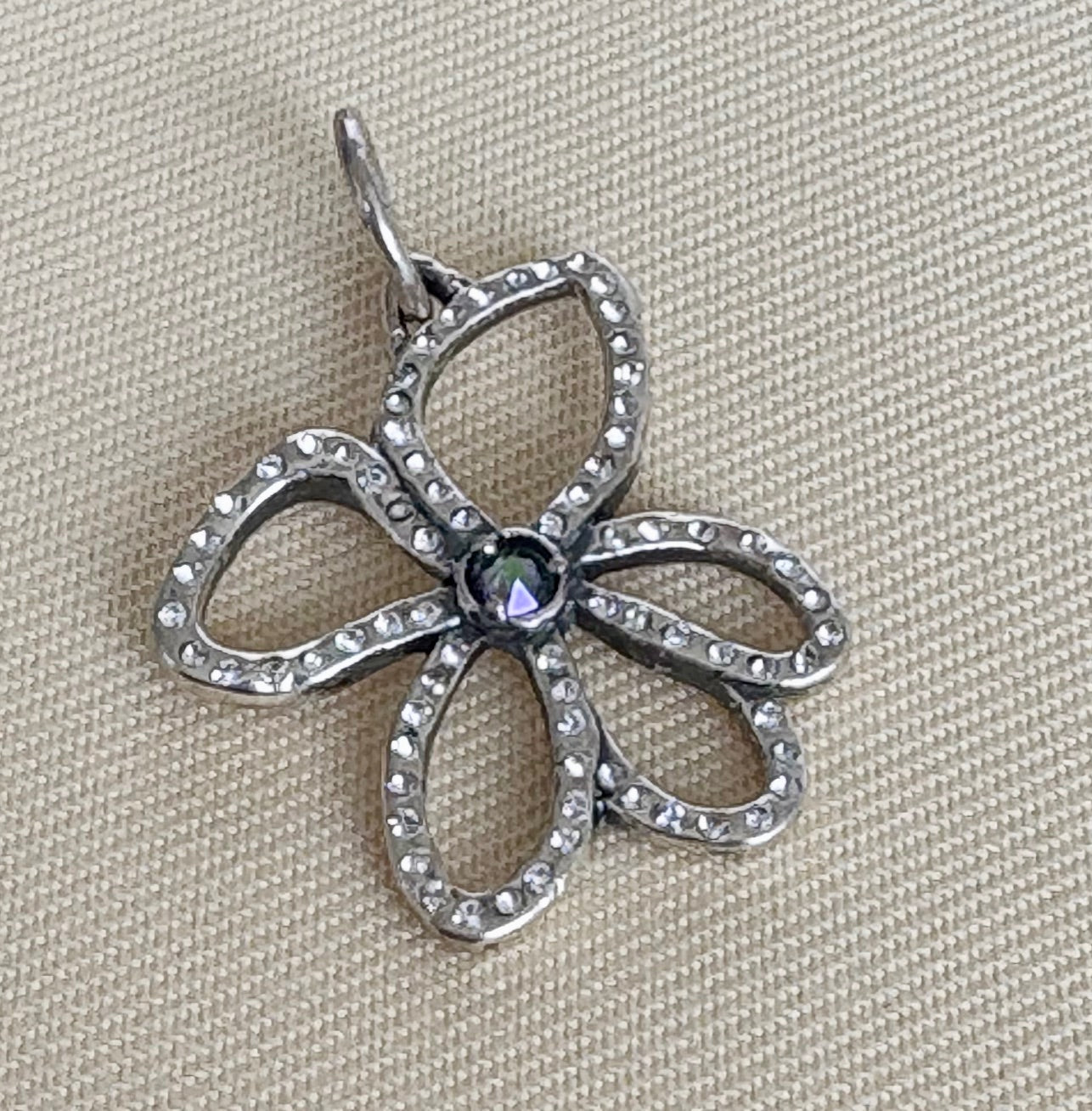 Sterling silver flower-shaped pendant with crystals on a beige fabric background