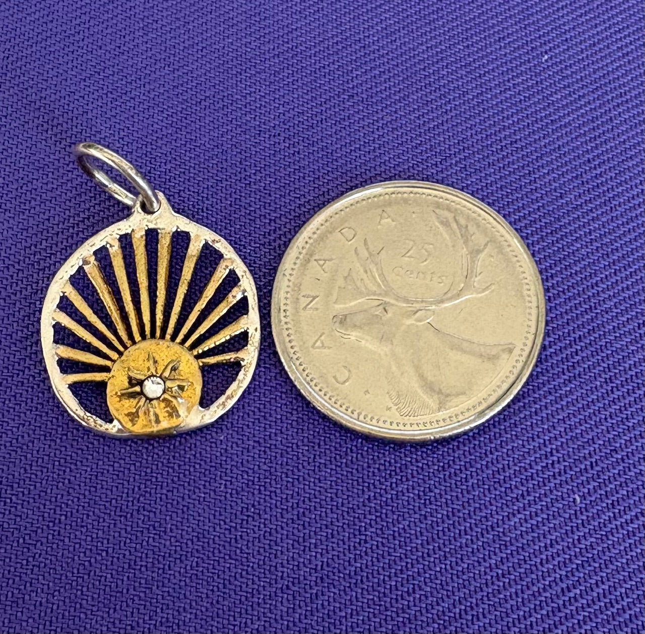 Gold and silver charm next to a Canadian coin on a blue background