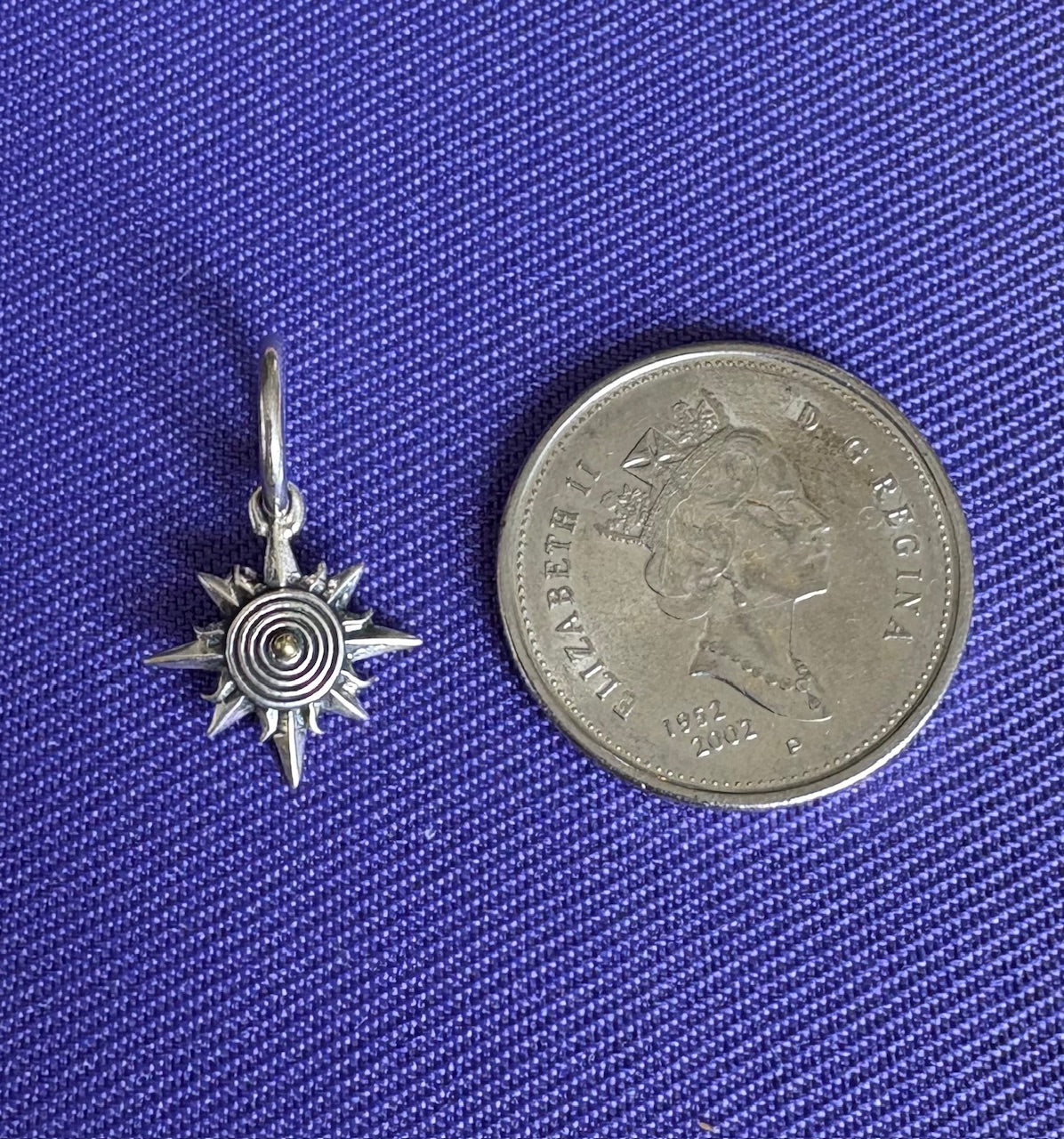Silver sun-shaped pendant next to a coin on a blue textured background