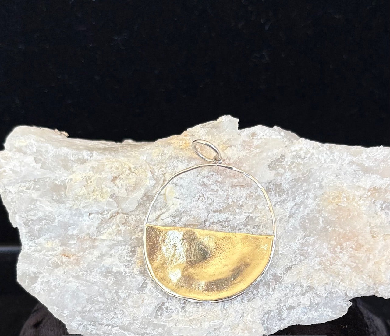 Waxing Poetic brass and silver pendant on a rock with a black background
