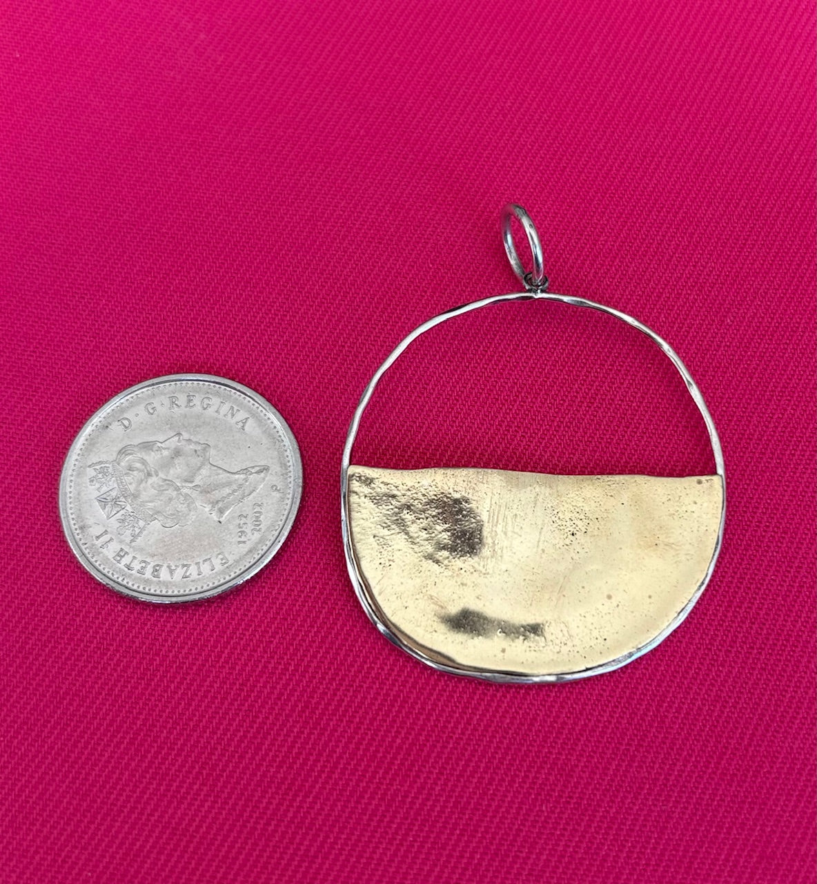 Gold and silver pendant next to a quarter on a pink background