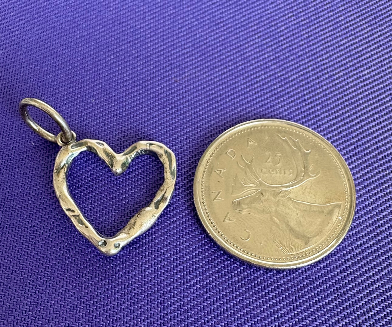 Silver heart-shaped charm pendant next to a coin on a blue fabric background. Waxing Poetic