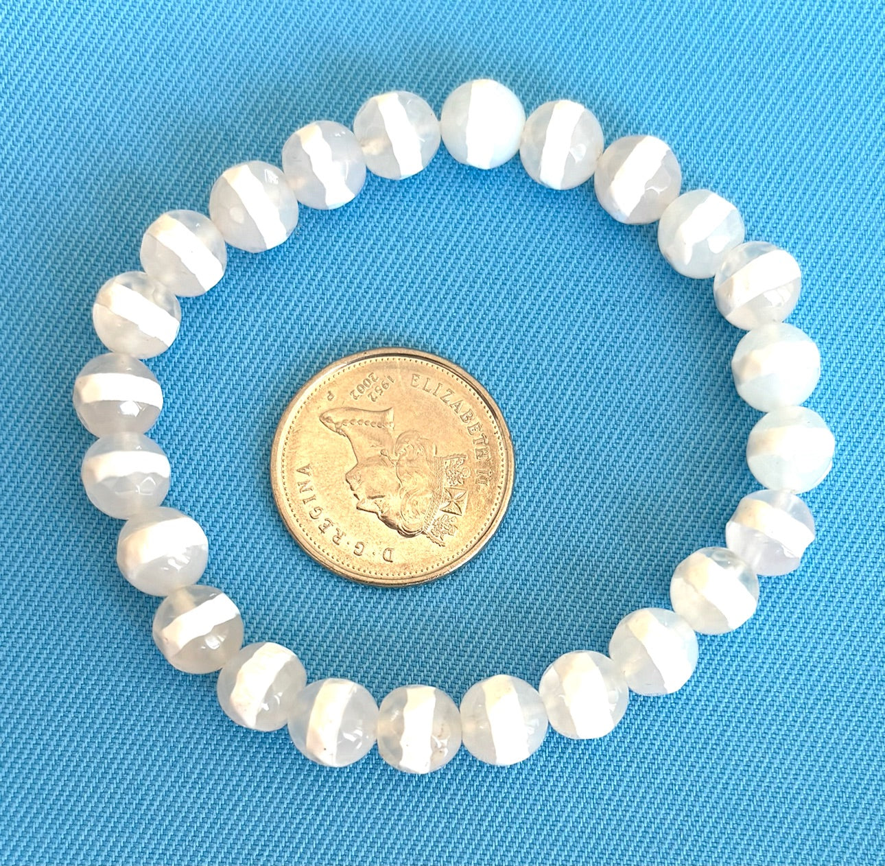 White striped agate bracelet on a blue background with a coin for size comparison