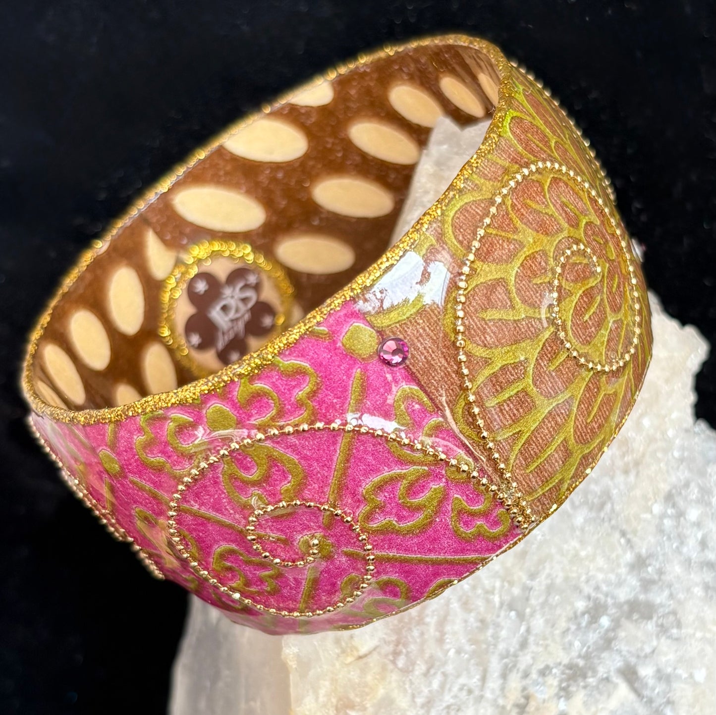Decorative bangle with pink and gold patterns on a black background