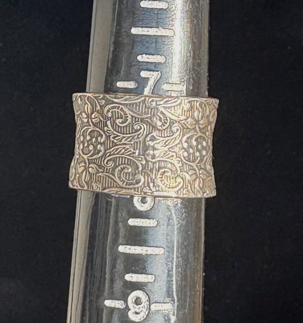 Embossed sterling silver ring against black background
