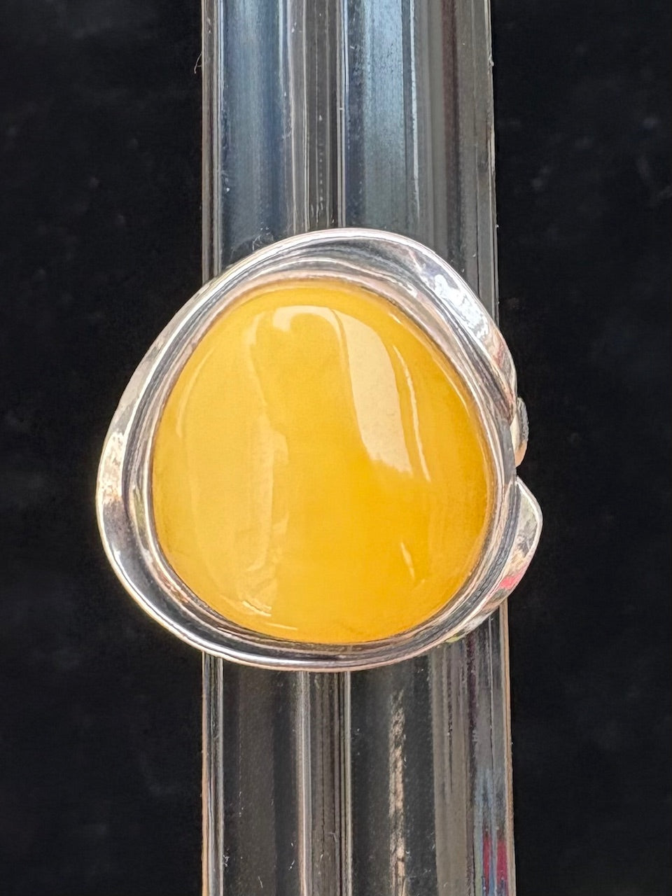 Ring with a butter yellow amber stone and silver band on a black background