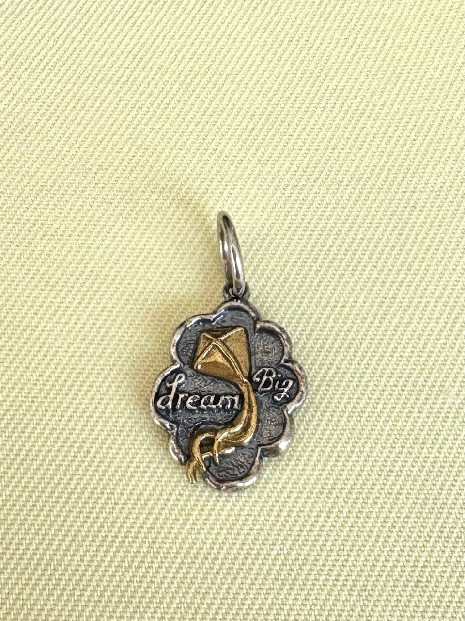 Waxing Poetic silver and gold pendant with 'dream Big' text on a beige fabric background