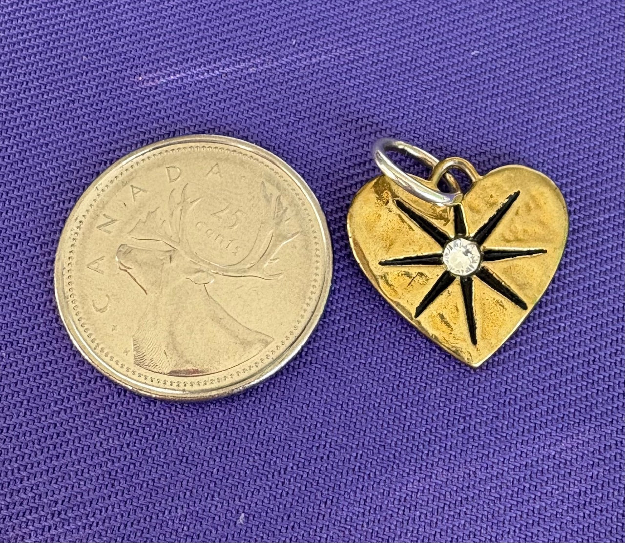 Gold heart-shaped pendant charm with star design next to a Canadian coin on a purple background